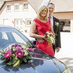 Vor ihren geschmückten Wagen posieren Braut und Bräutigam
