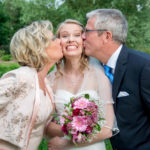 Mutter und Vater küssen die Braut an ihrer Hochzeit